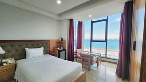 A hotel room with a large bed, a desk with a lamp, a chair, and a view of the beach. - Happy Light Central Nha Trang (Nha Trang)