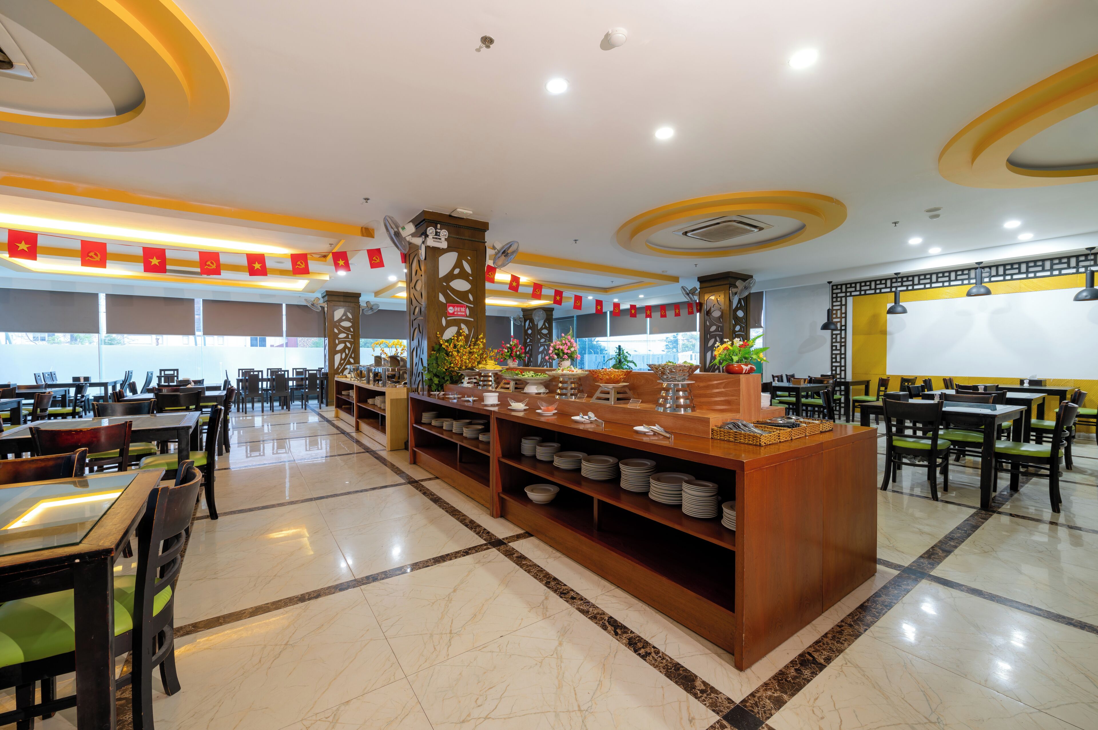 A spacious restaurant with multiple dining tables and chairs, a central buffet area with various dishes, and a clean, well-lit interior.