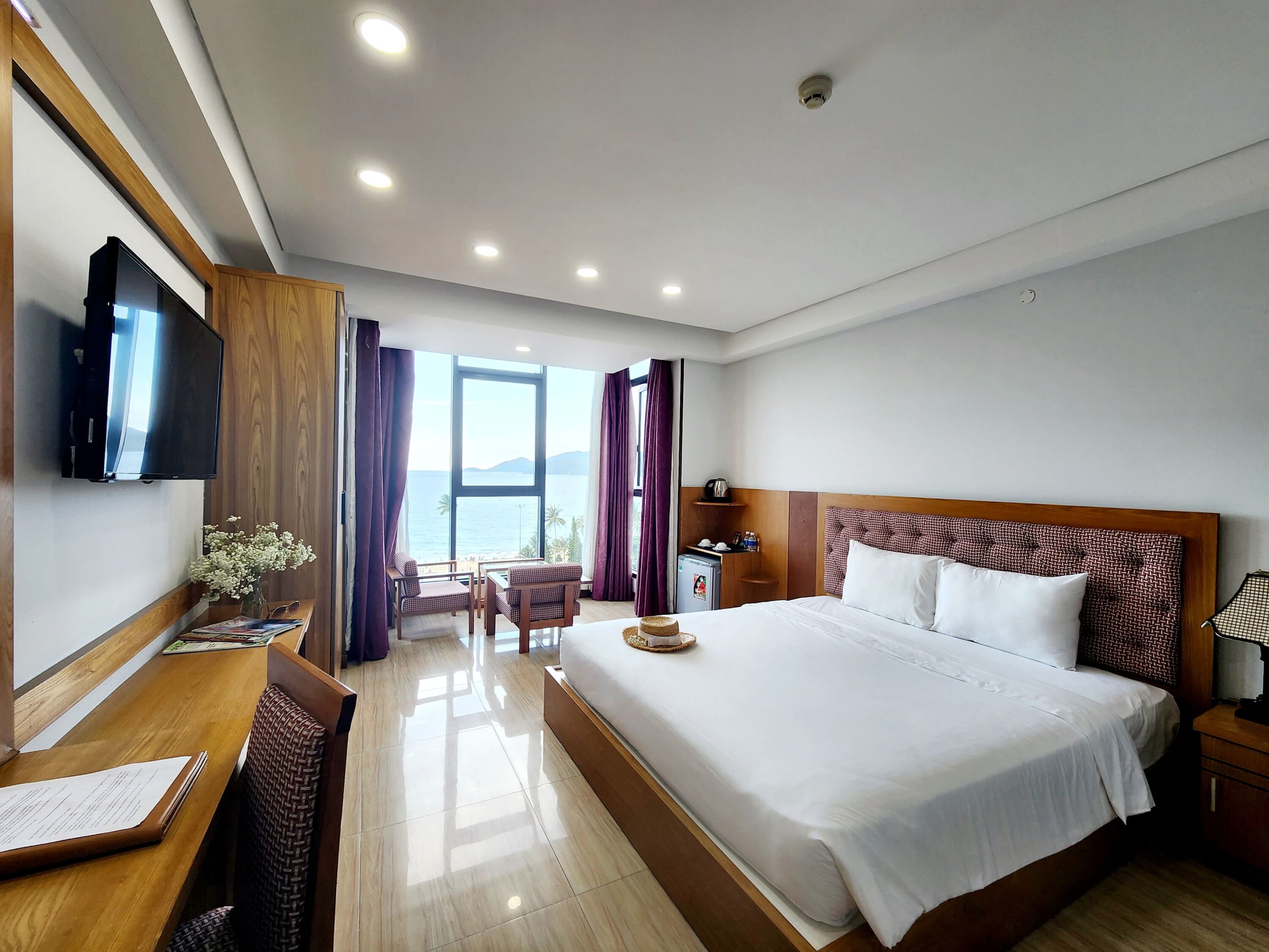 Une chambre d’hôtel avec un grand lit, un bureau avec une chaise, une télévision et une vue sur la mer.