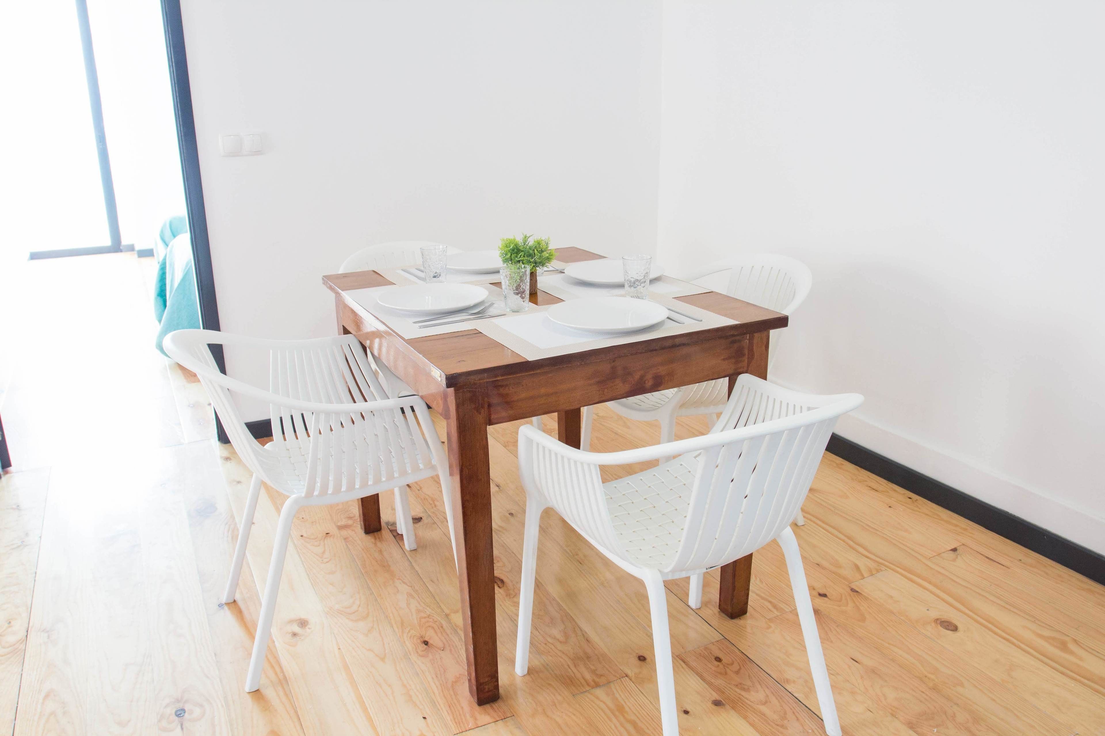 Una mesa de comedor con sillas blancas, una planta pequeña y platos y vasos blancos.