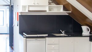 A compact kitchen with white cabinets, a black countertop, and a small refrigerator.