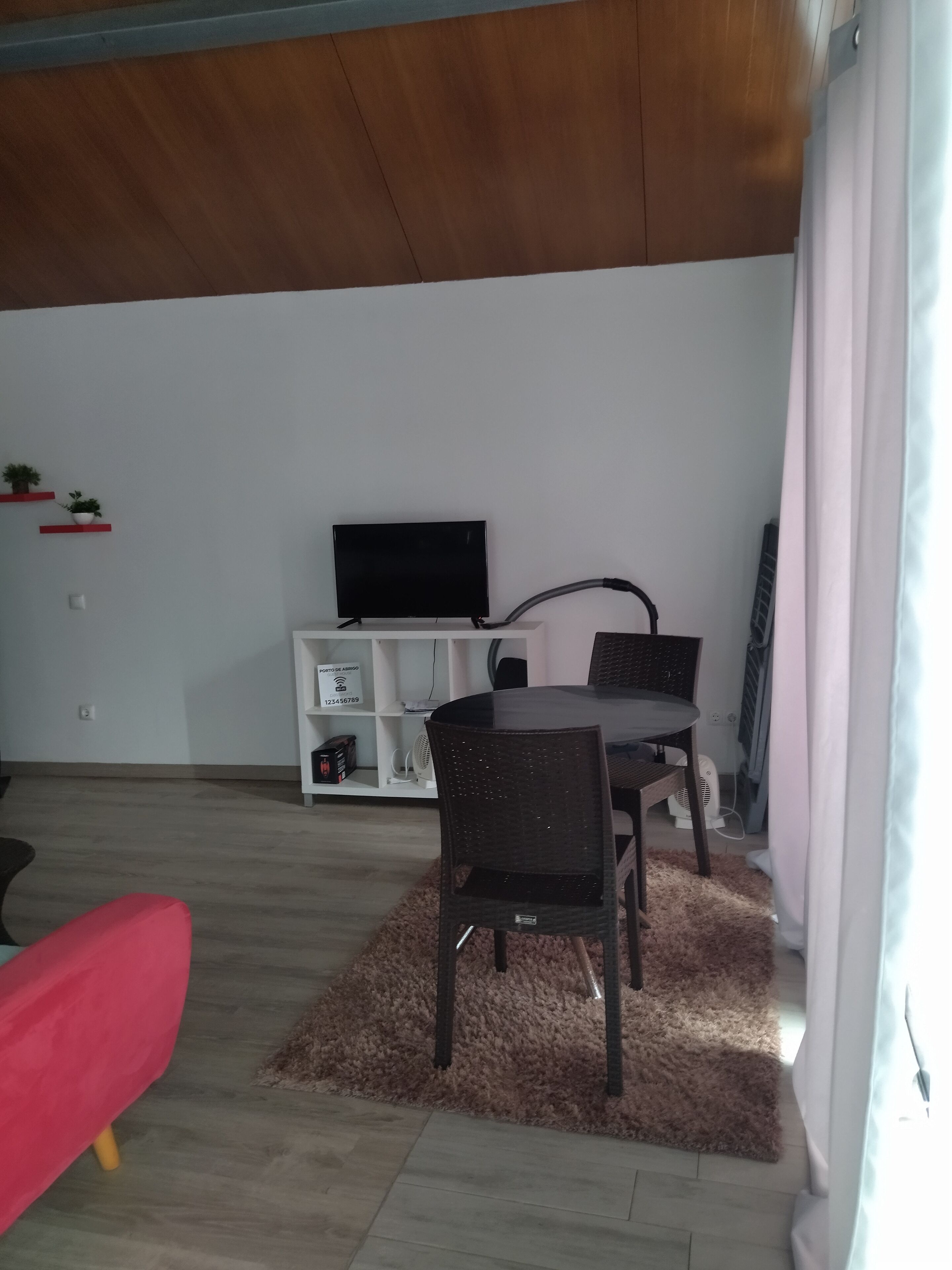 En stue med et fjernsyn på et hvidt skærmstativ, et spisebord med stole, en rød sofa og en bl ød måtte.