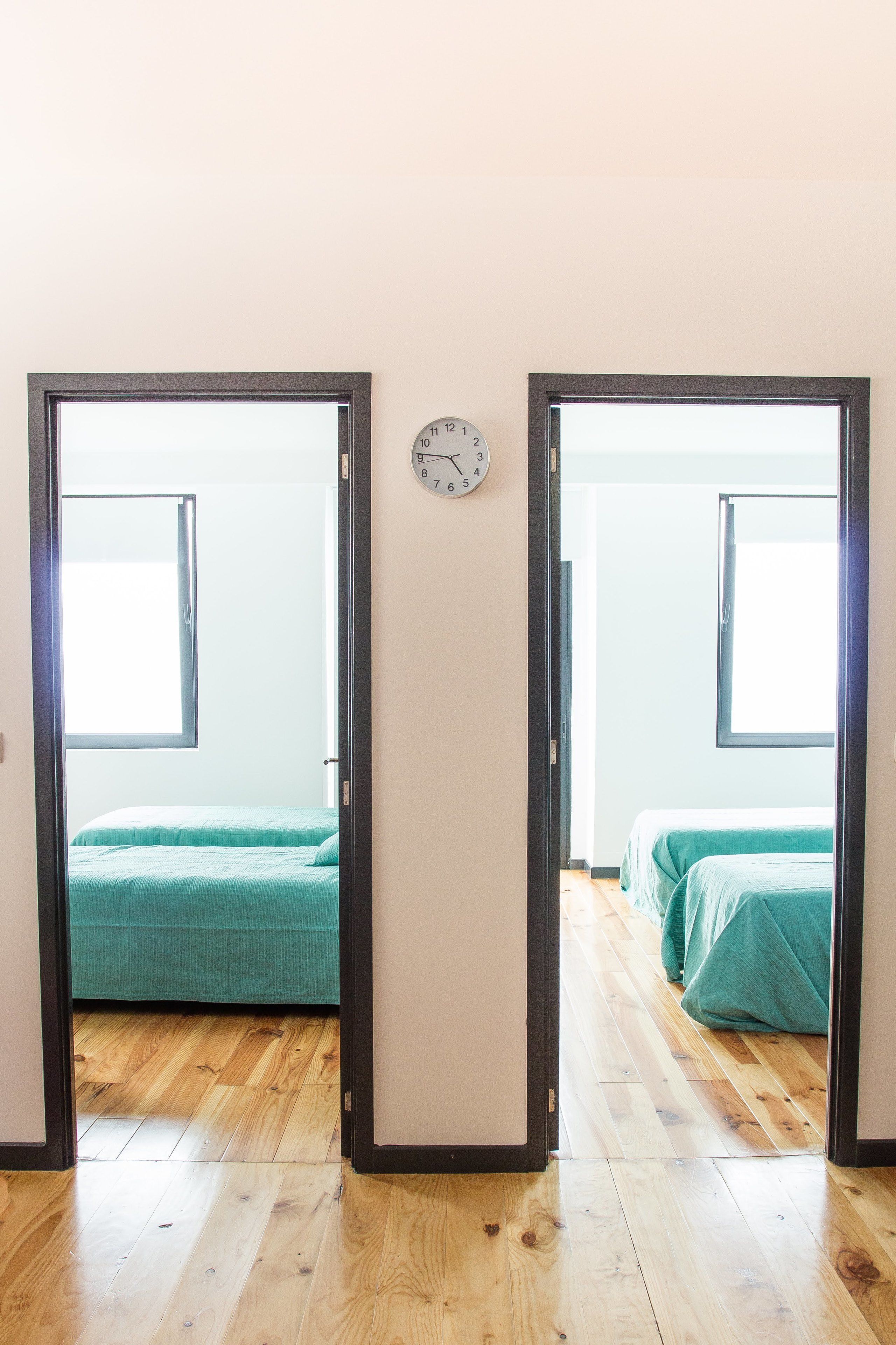 A room with two beds, wooden flooring, and a wall clock.