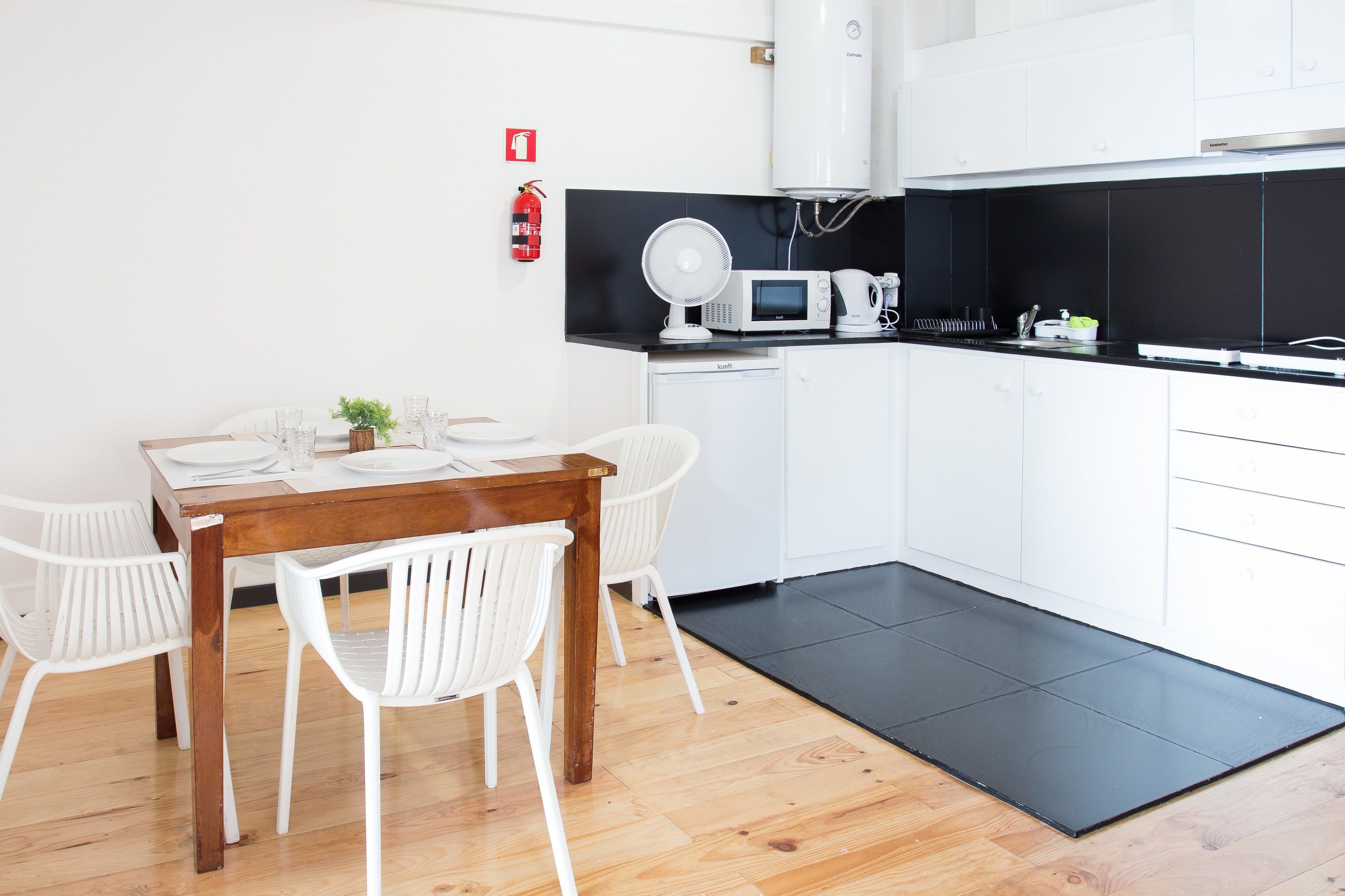 A modern kitchen with white cabinets, a black countertop, a microwave, a coffee maker, and a fire extinguisher on the wall.