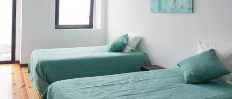 A room with two beds, each with a green bedspread and pillows, a window, and a cactus-themed wall decoration.