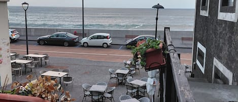 Un patio frente al mar con mesas al aire libre, vista al océano y coches estacionados.