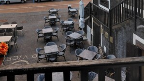 A seaside terrace with outdoor seating, a building with large windows, and a view of the ocean.