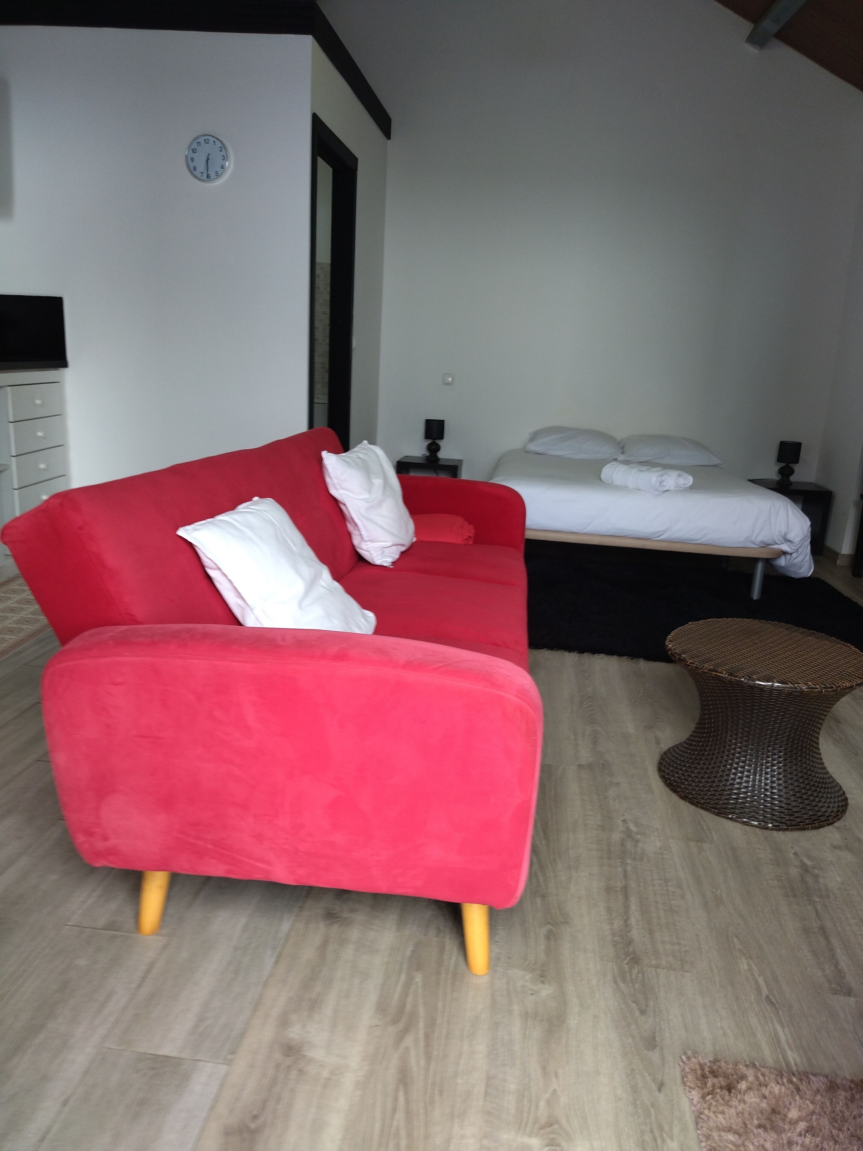 Une chambre d’hôtel avec un canapé rouge, un lit avec une literie blanche, une petite table et une horloge au mur.