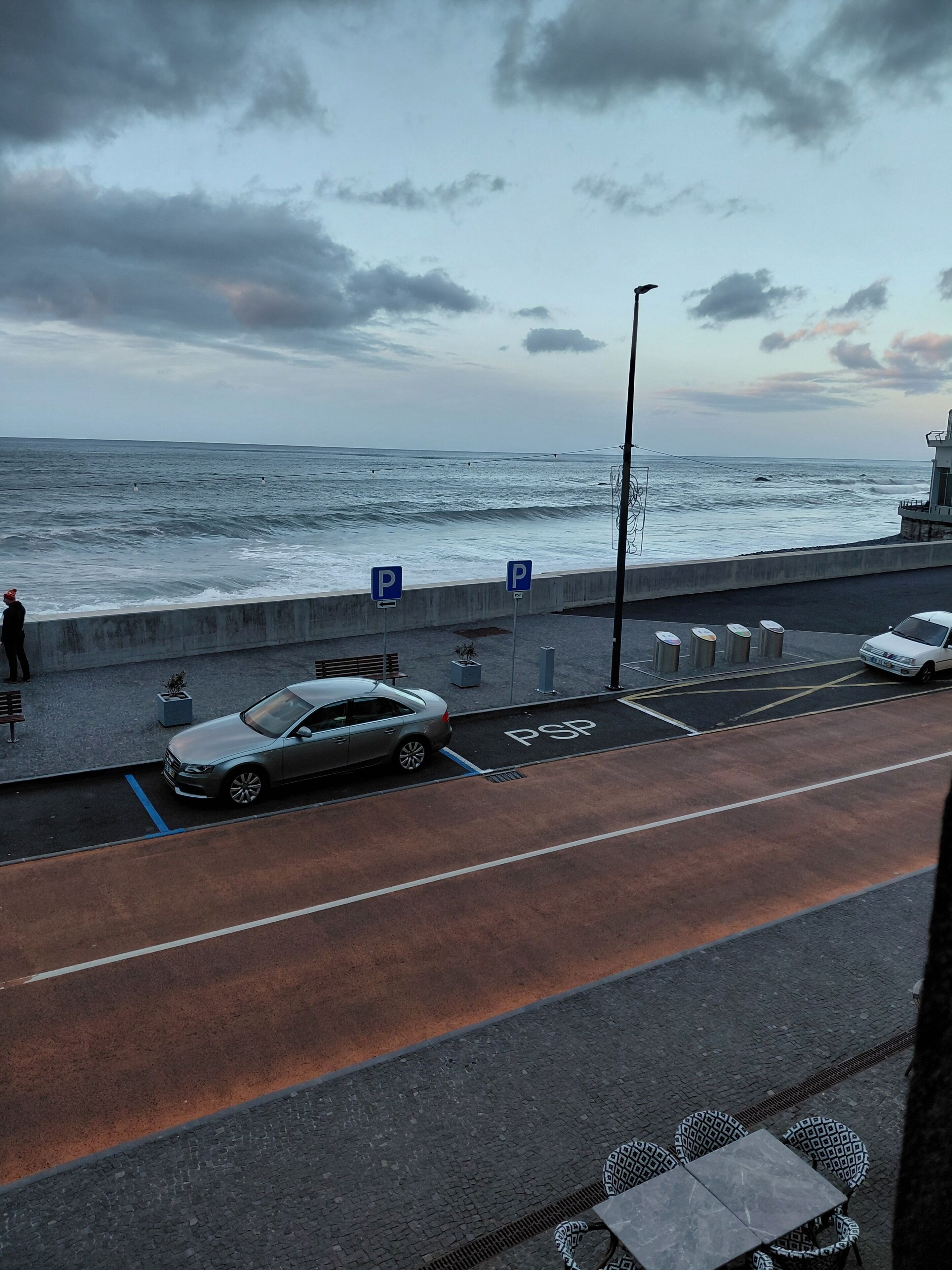 A coastal parking area with a view of the sea, a car, and a bench.