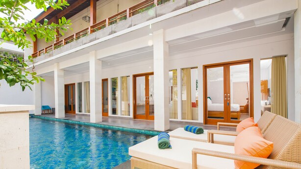 Ett område vid poolen med solstolar, en pool och en överbyggd gångväg med en balkong.