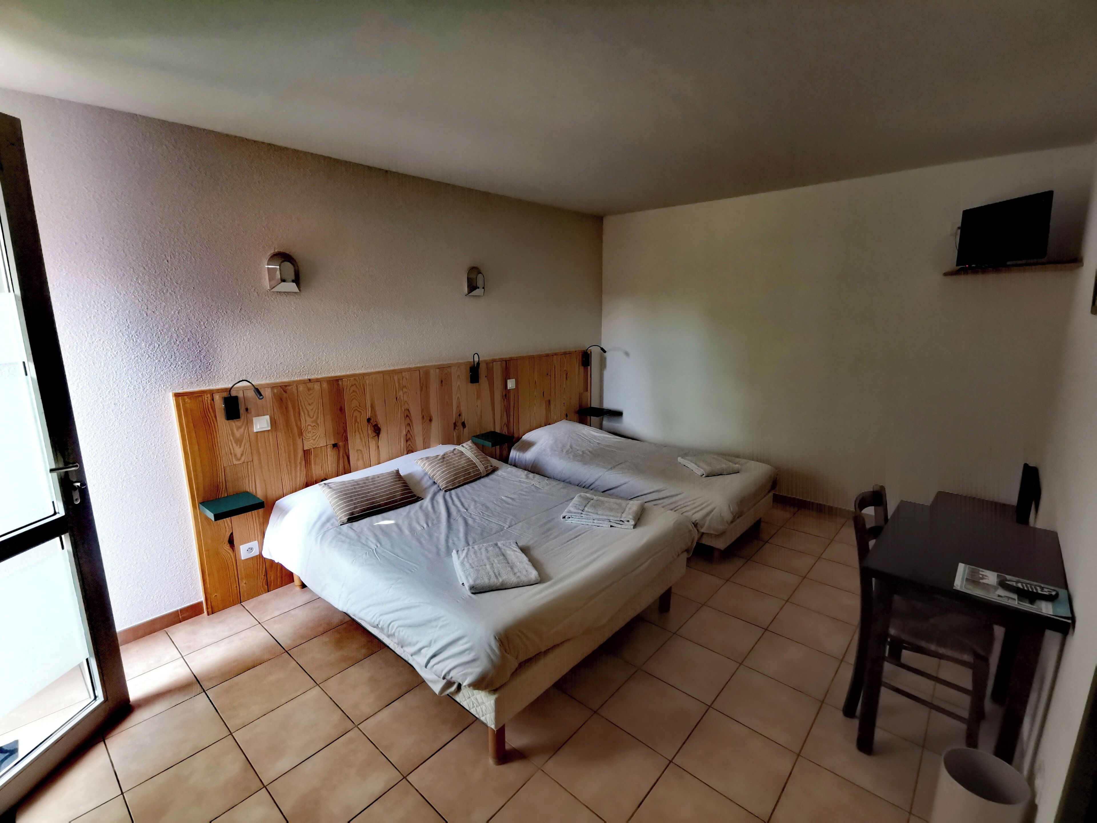 Een slaapkamer met twee bedden, een houten hoofdbord, een klein tafeltje en een televisie aan de muur.