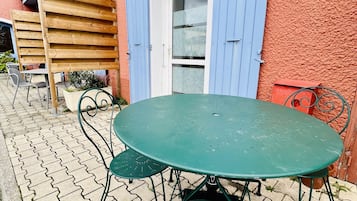Una mesa y sillas de metal verde sobre un patio empedrado, con un edificio rojo al fondo.