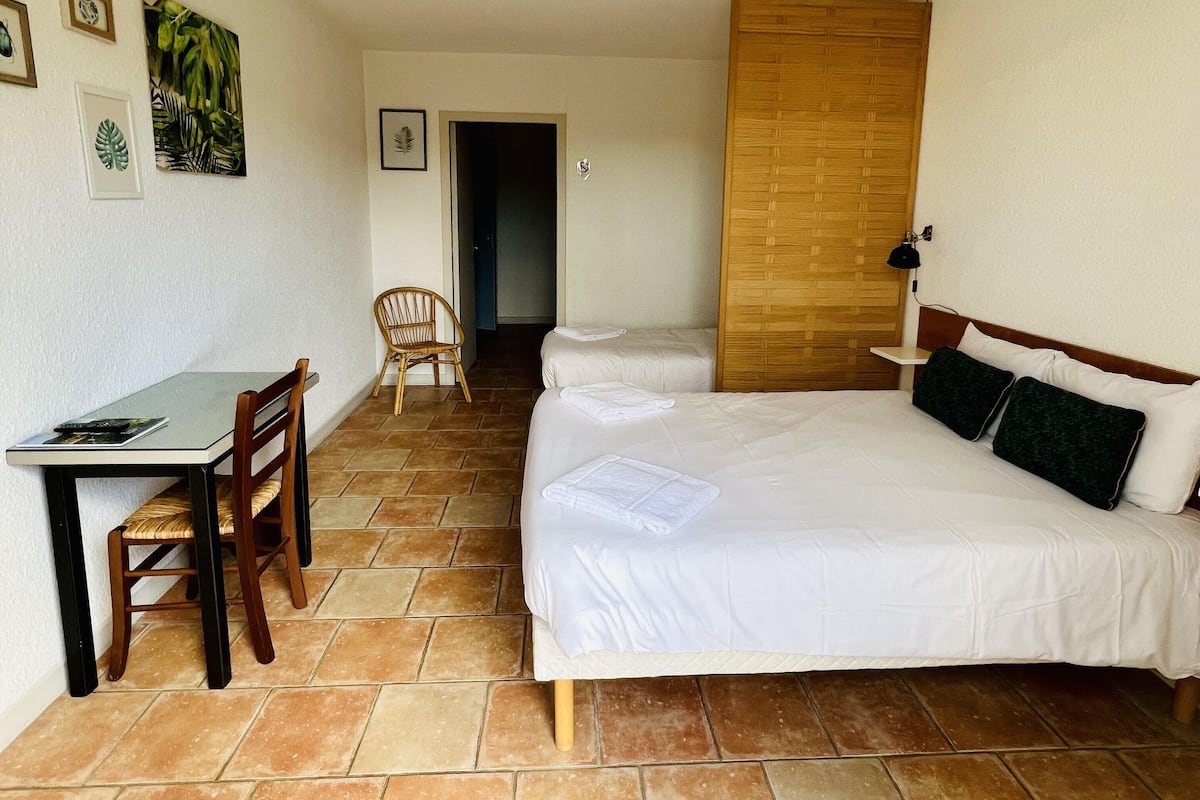 A room with a bed, a desk, and a chair. There are framed pictures on the wall.
