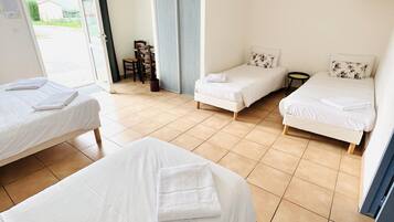 Habitación de hotel con tres camas, una silla, una mesita pequeña y una puerta corredera que da a un balcón.