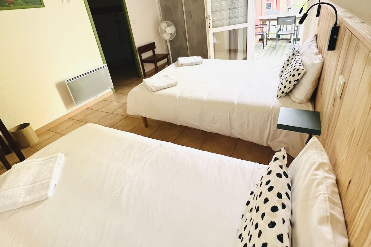 A hotel room with two beds, a small table, a chair, and a view of the outside.