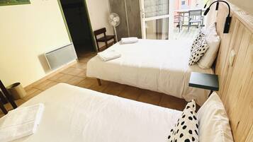 A hotel room with two beds, a small table, a chair, and a view of the outside.