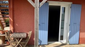 Una mesa y sillas de madera frente a un edificio con fachada roja y contraventanas azules.