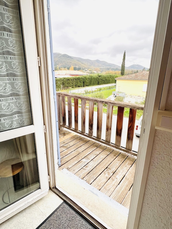 A balcony with a wooden floor, a metal railing, and a view of a green landscape with mountains in the distance. - Hotel Rose des vents (Baix)