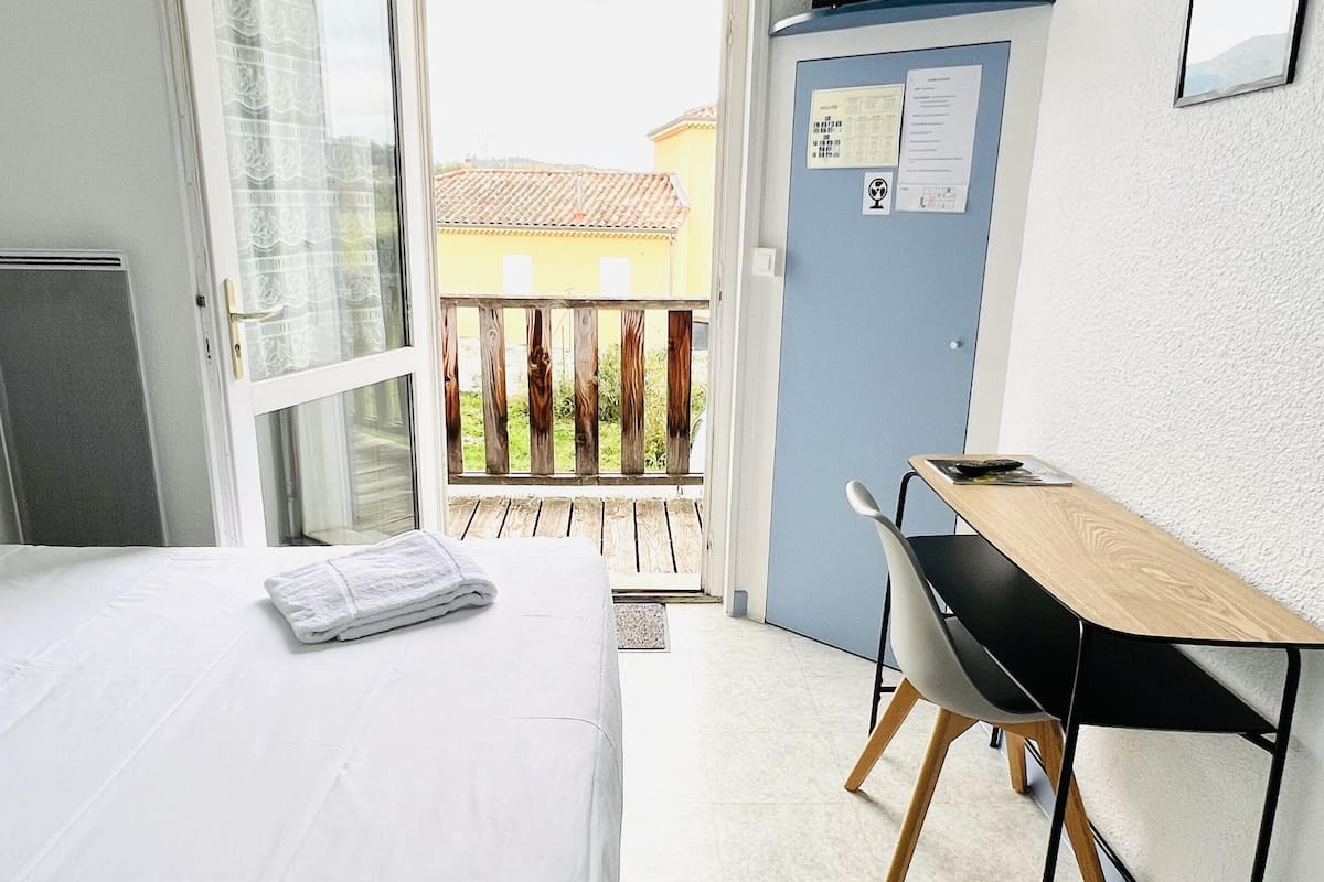 A hotel room with a bed, a desk, a chair, a television, and a view of the outside.