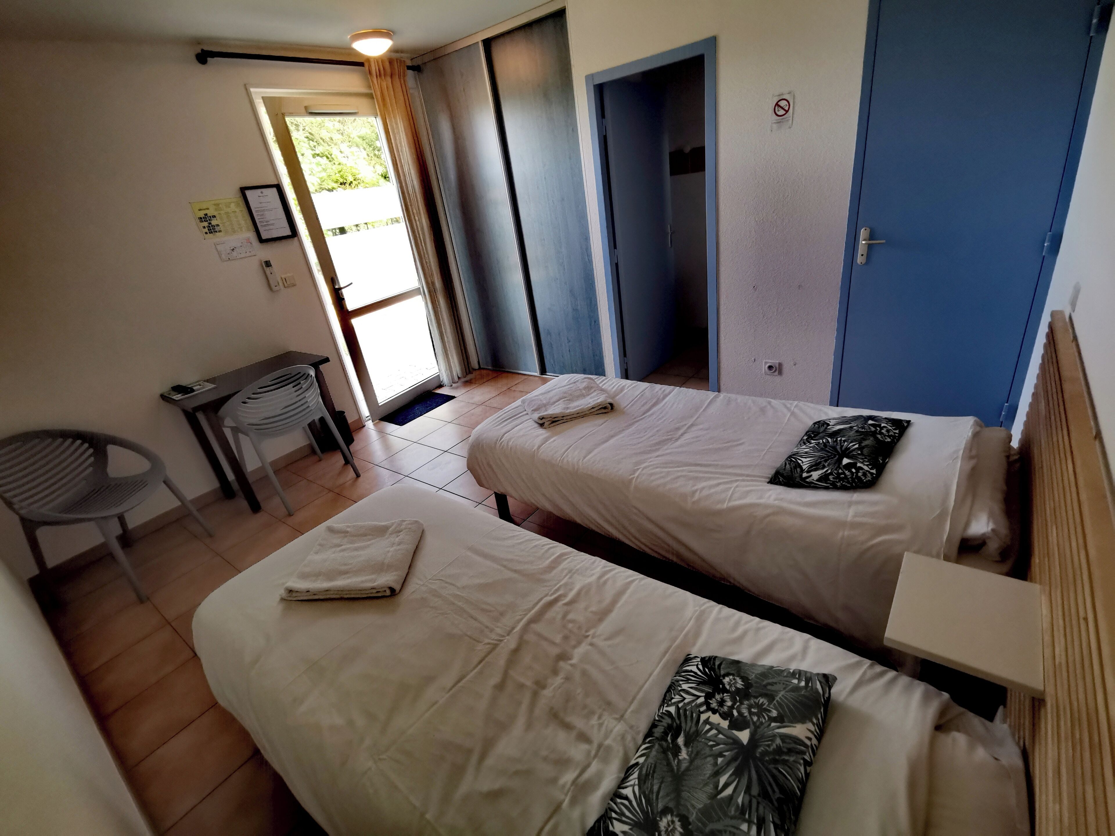 A hotel room with two beds, a desk, a chair, and a door.