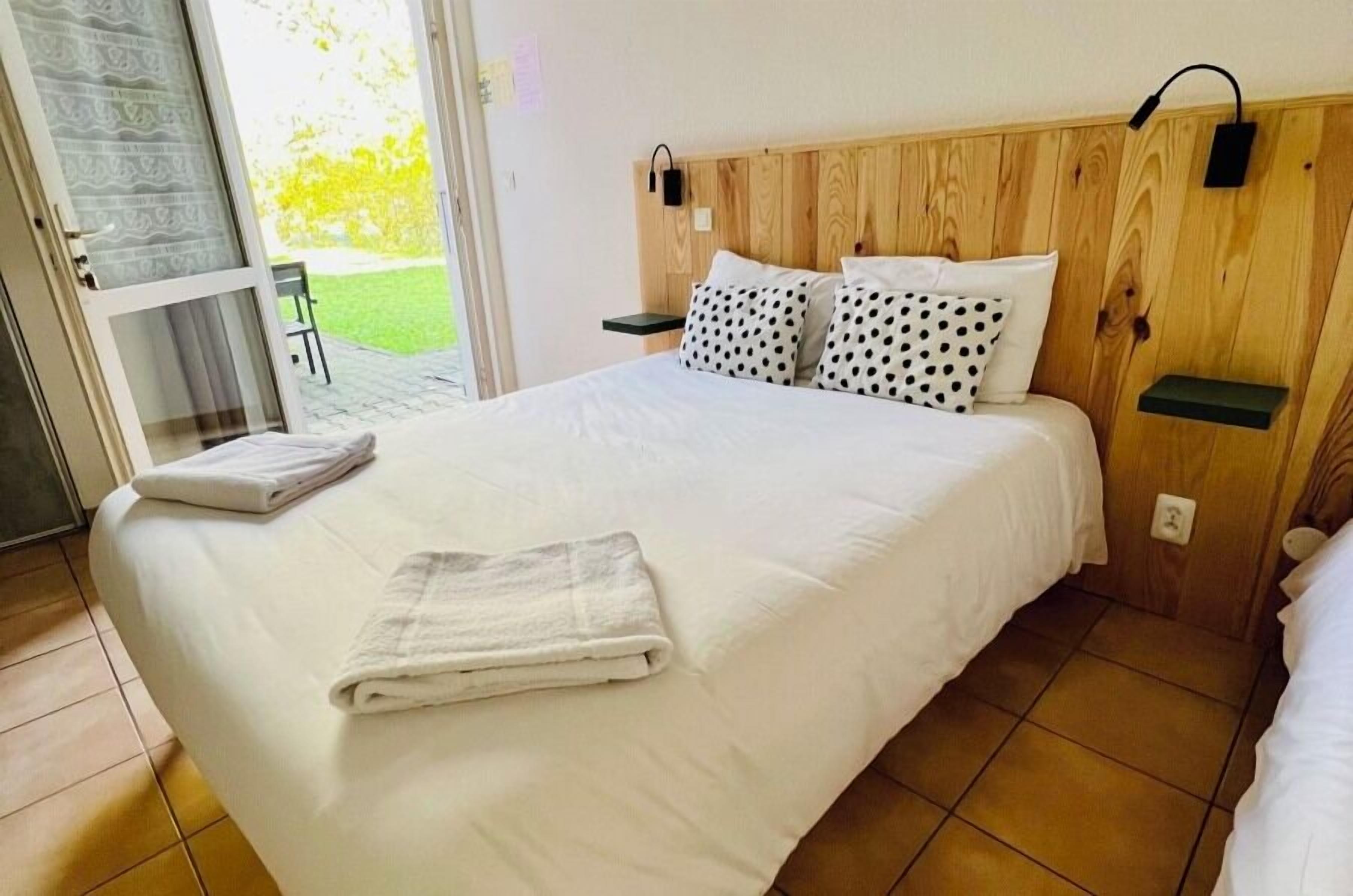 Quarto de hotel com uma cama grande, duas mesas de cabeceira, um painel de madeira e vista para um jardim por uma porta deslizante.
