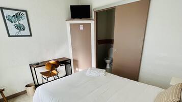 A hotel room with a bed, a desk, a chair, a television, and a toilet.