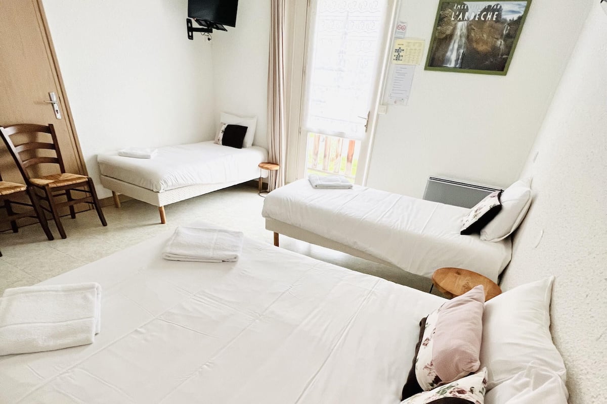 A hotel room with two beds, a TV mounted on the wall, a window with curtains, and a poster on the wall.