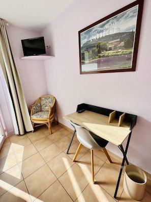 Una habitación con un escritorio de madera, una silla, un televisor montado en la pared y un cuadro con un paisaje.