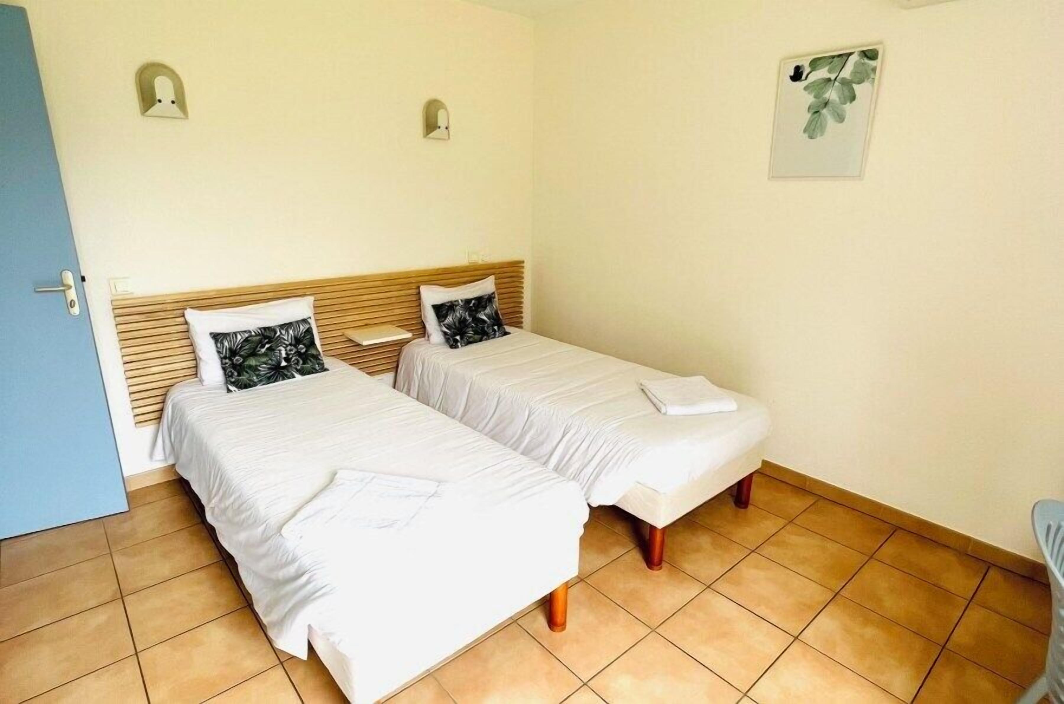 A room with two beds, a blue door, and a wall-mounted light fixture.