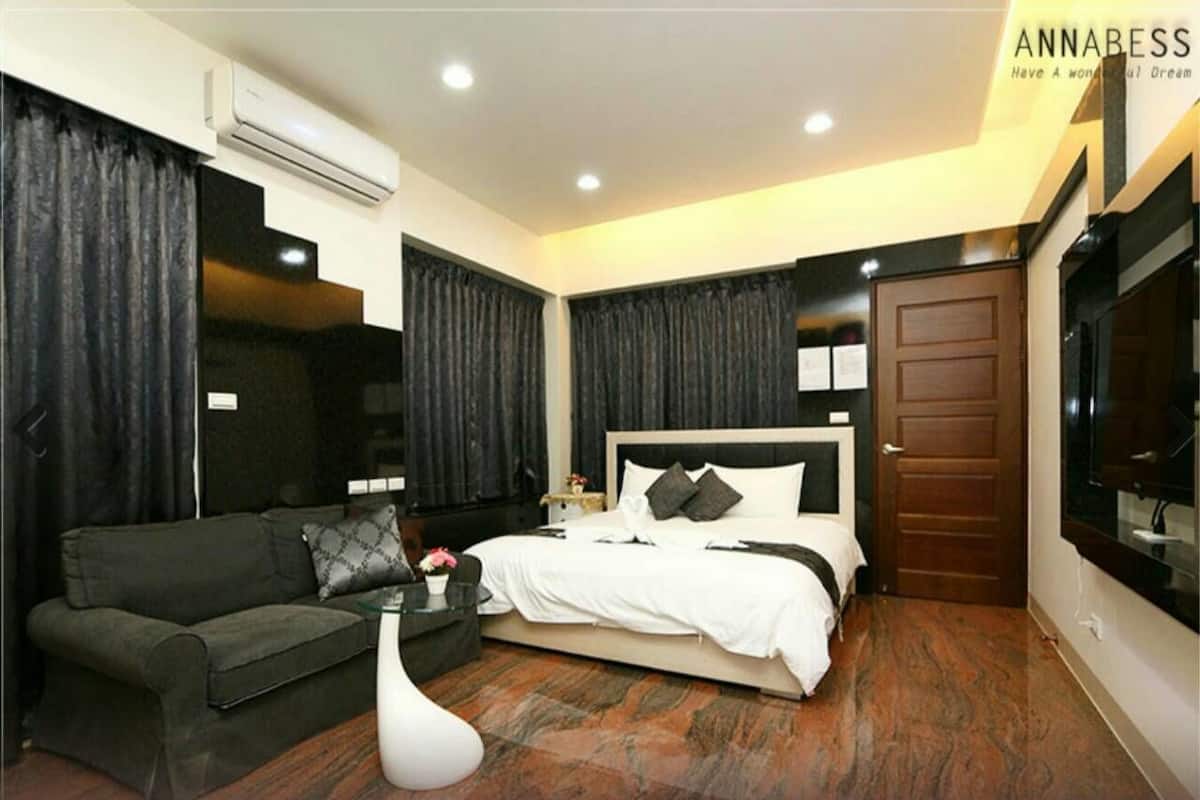 A modern hotel room with a large bed, a sofa, a small table, and a TV.