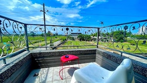 A balcony with a white plastic chair and a red table, overlooking a green landscape with a clear blue sky. - Annabess (Wujie)