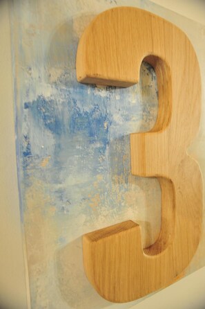 A wooden number '3' mounted on a wall with a textured blue and white background.