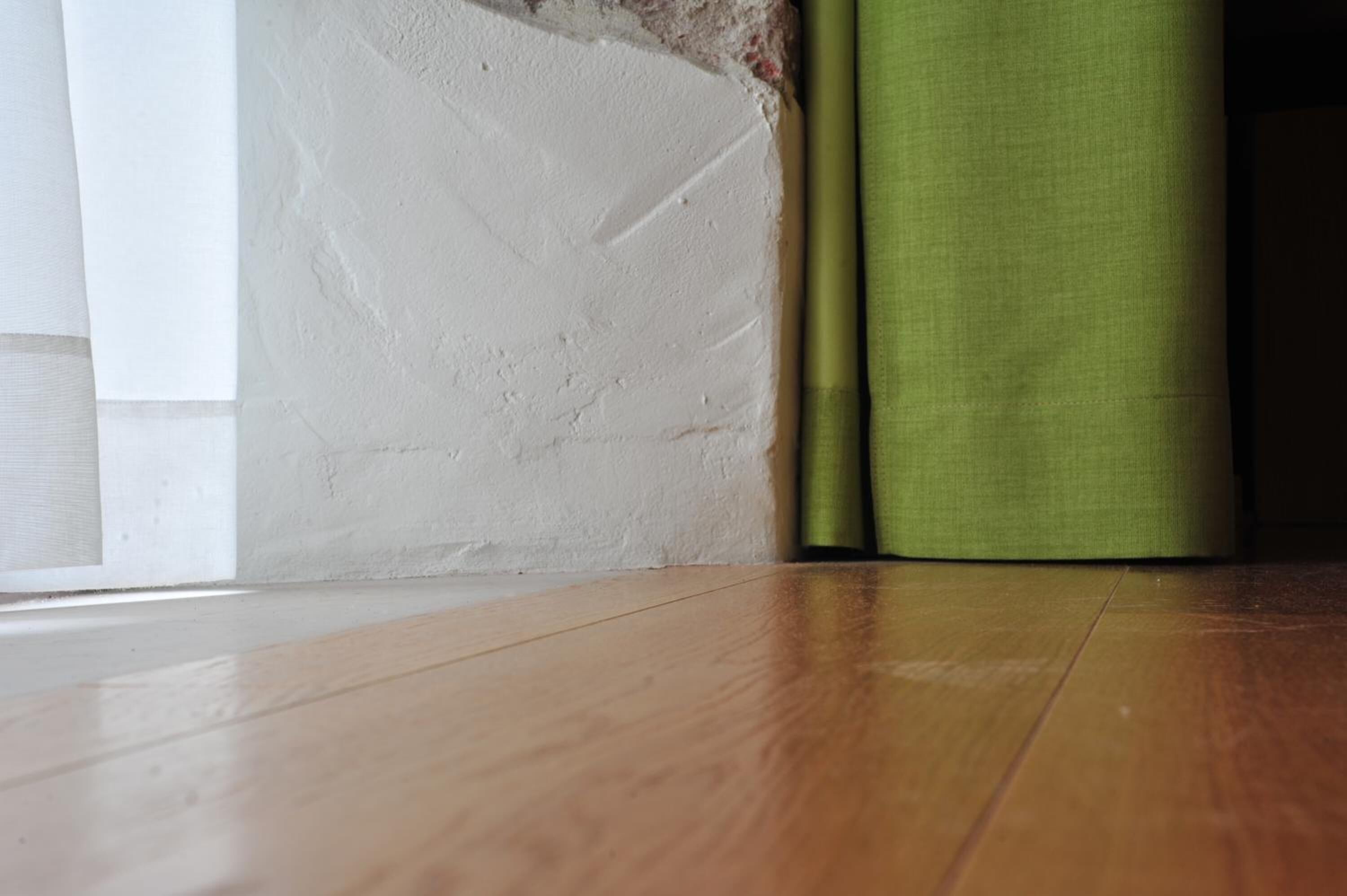 A wooden floor, a white wall with a rough texture, and a green fabric object.