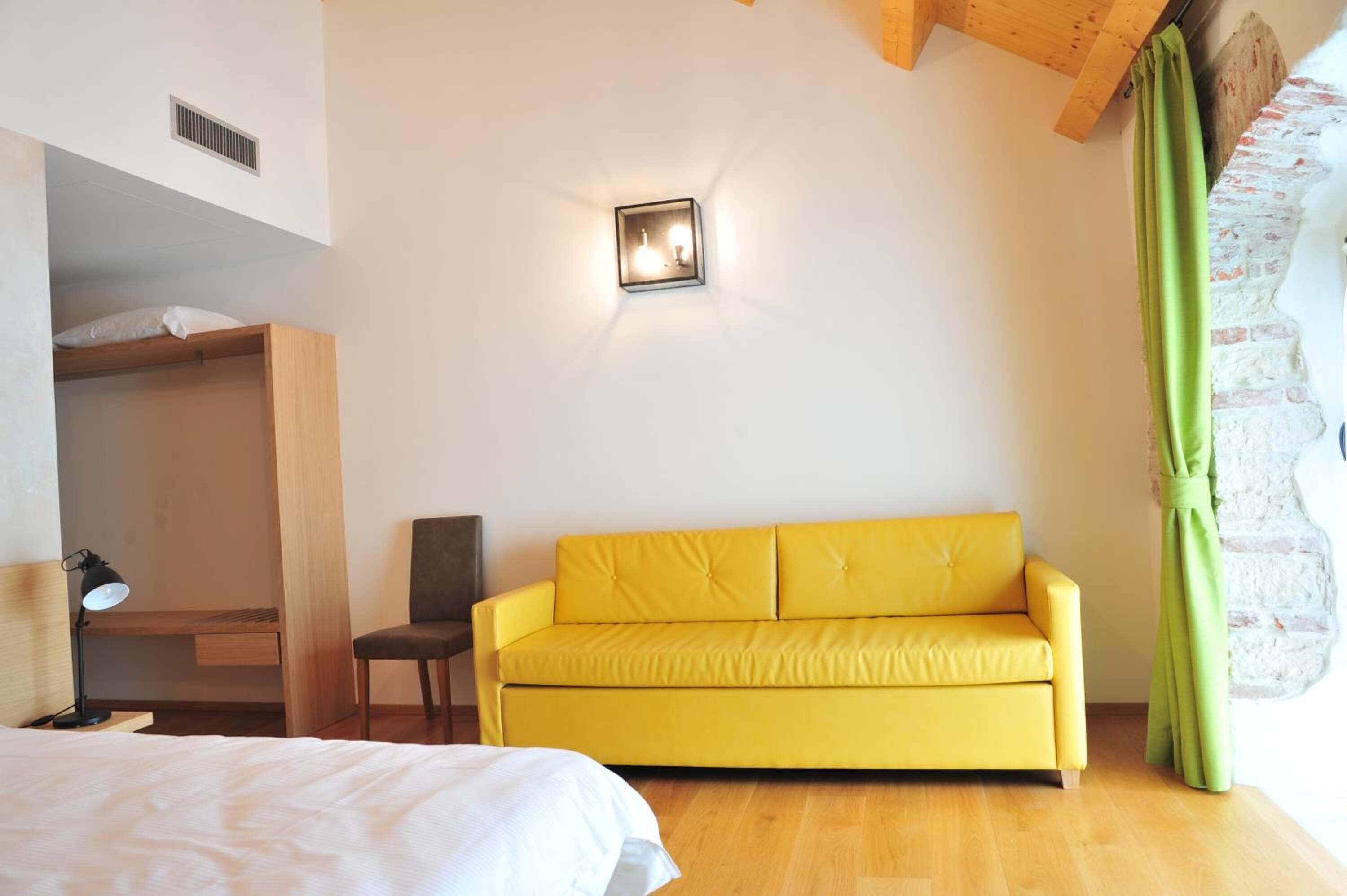 Une pièce avec un canapé jaune, un bureau en bois, une chaise et un lit.