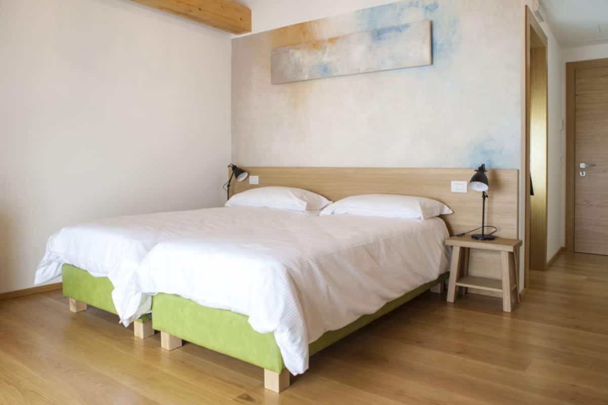 A bedroom with a wooden bed frame, two bedside tables with lamps, a green upholstered bench, and a painting on the wall.