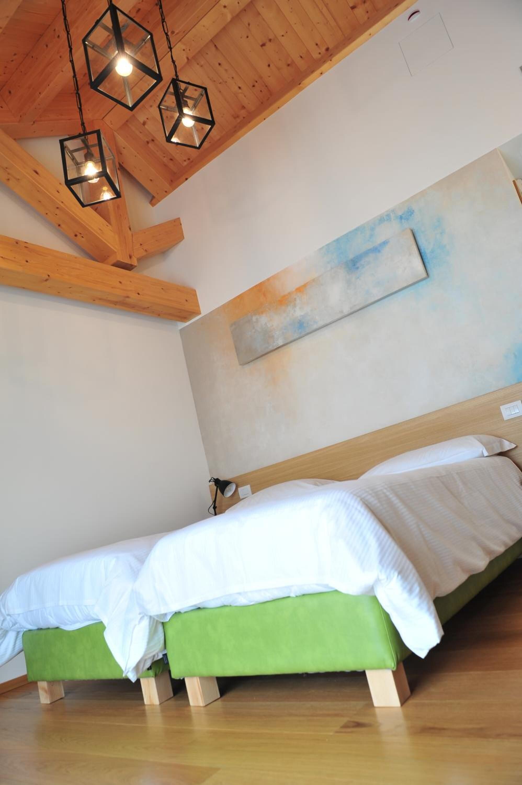 A bedroom with a wooden ceiling, a green bed, and a large abstract painting on the wall.