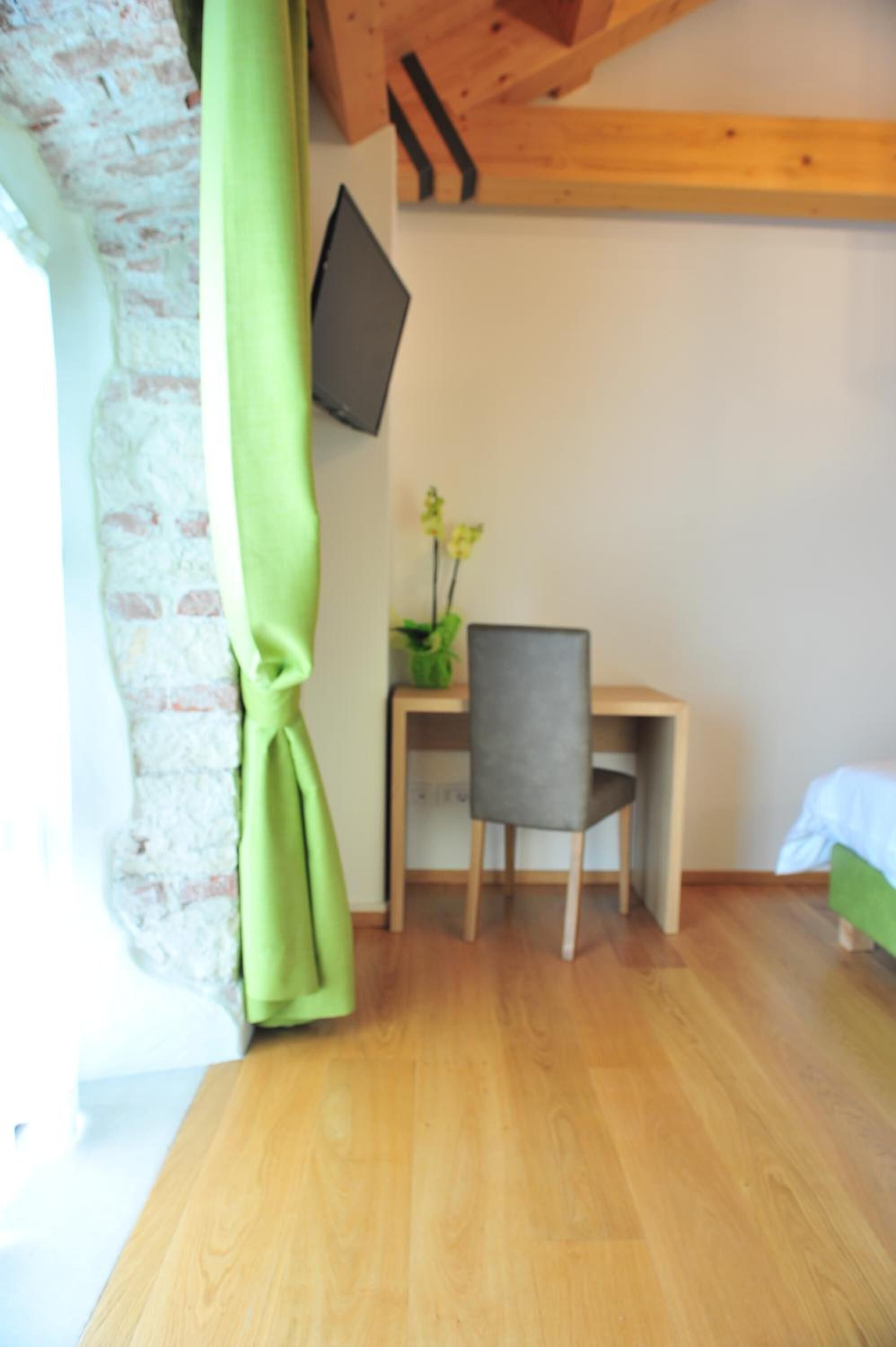 Una habitación con un escritorio de madera, una silla, una planta pequeña y un televisor montado en la pared.