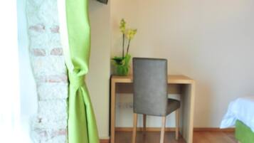 Una habitación con un escritorio de madera, una silla, una planta pequeña y un televisor montado en la pared.