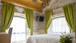 Une chambre avec un grand lit, des rideaux verts, un téléviseur à écran plat et un plafond en bois.