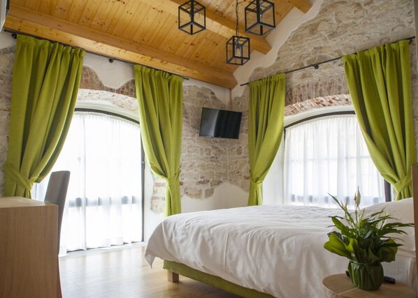 A bedroom with a large bed, green curtains, a flat-screen TV, and a wooden ceiling.
