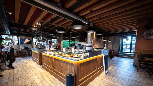Un restaurant doté d’un comptoir central, d’un plancher en bois et de conduits apparents au plafond.