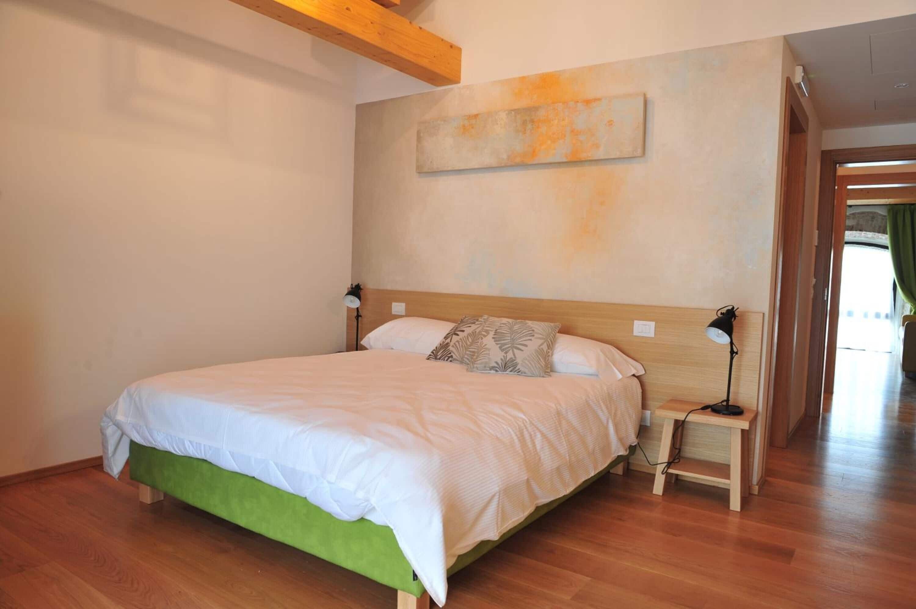 A bedroom with a large bed, bedside tables, a nightstand, and a painting on the wall.