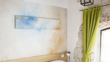 Quarto com cabeceira de madeira, colcha branca, mesa de cabeceira com abajur e cortina verde.