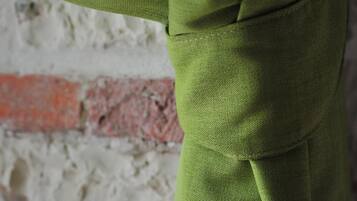 Un gros plan d’un tissu vert à la texture particulière, qui pourrait être un morceau de vêtement ou un revêtement d’ameublement, sur un fond constitué d’un mur brut et non fini, avec un motif de briques rouges.