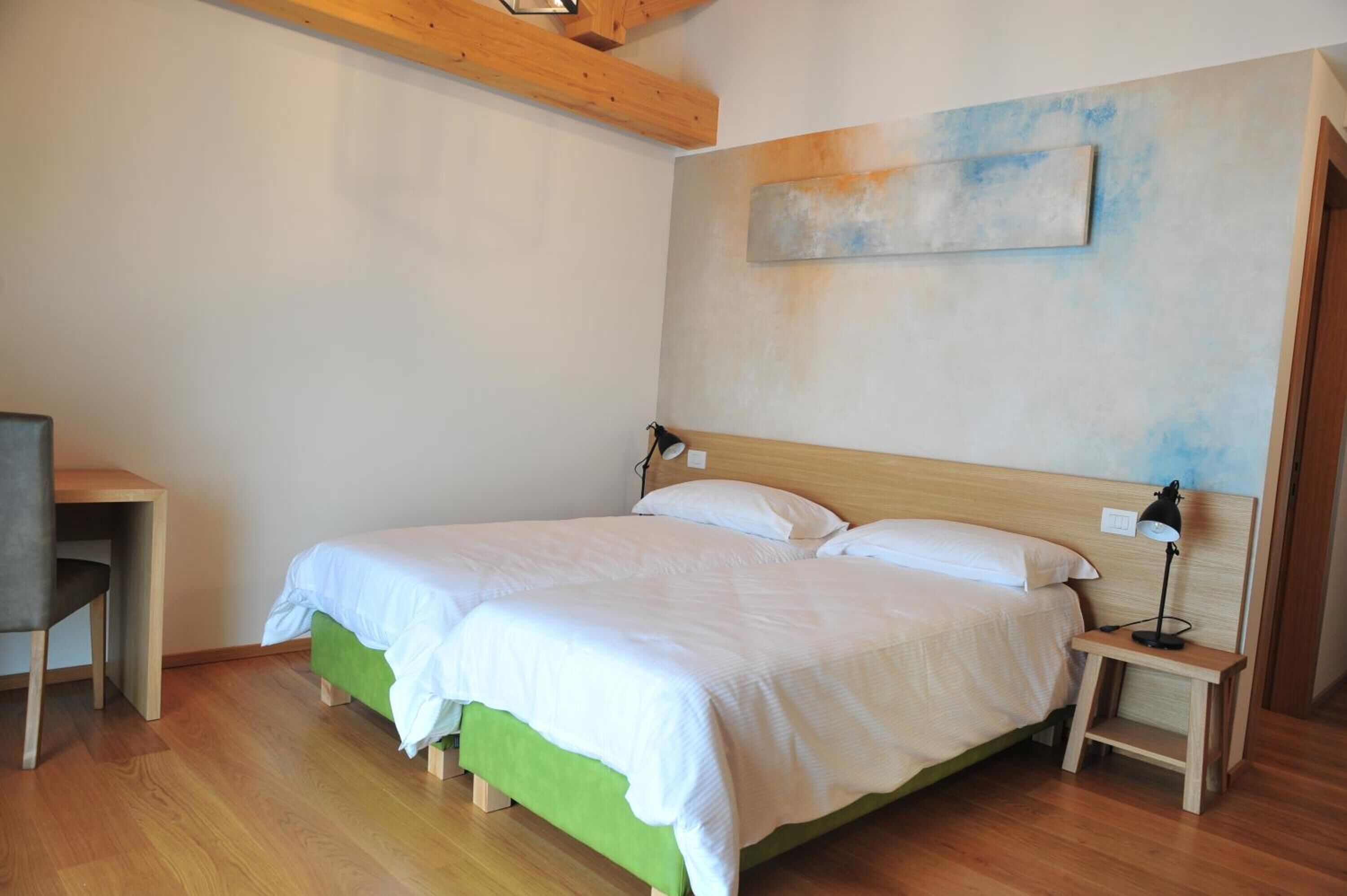 A bedroom with a double bed, a bedside table with a lamp, a chair, and a desk.