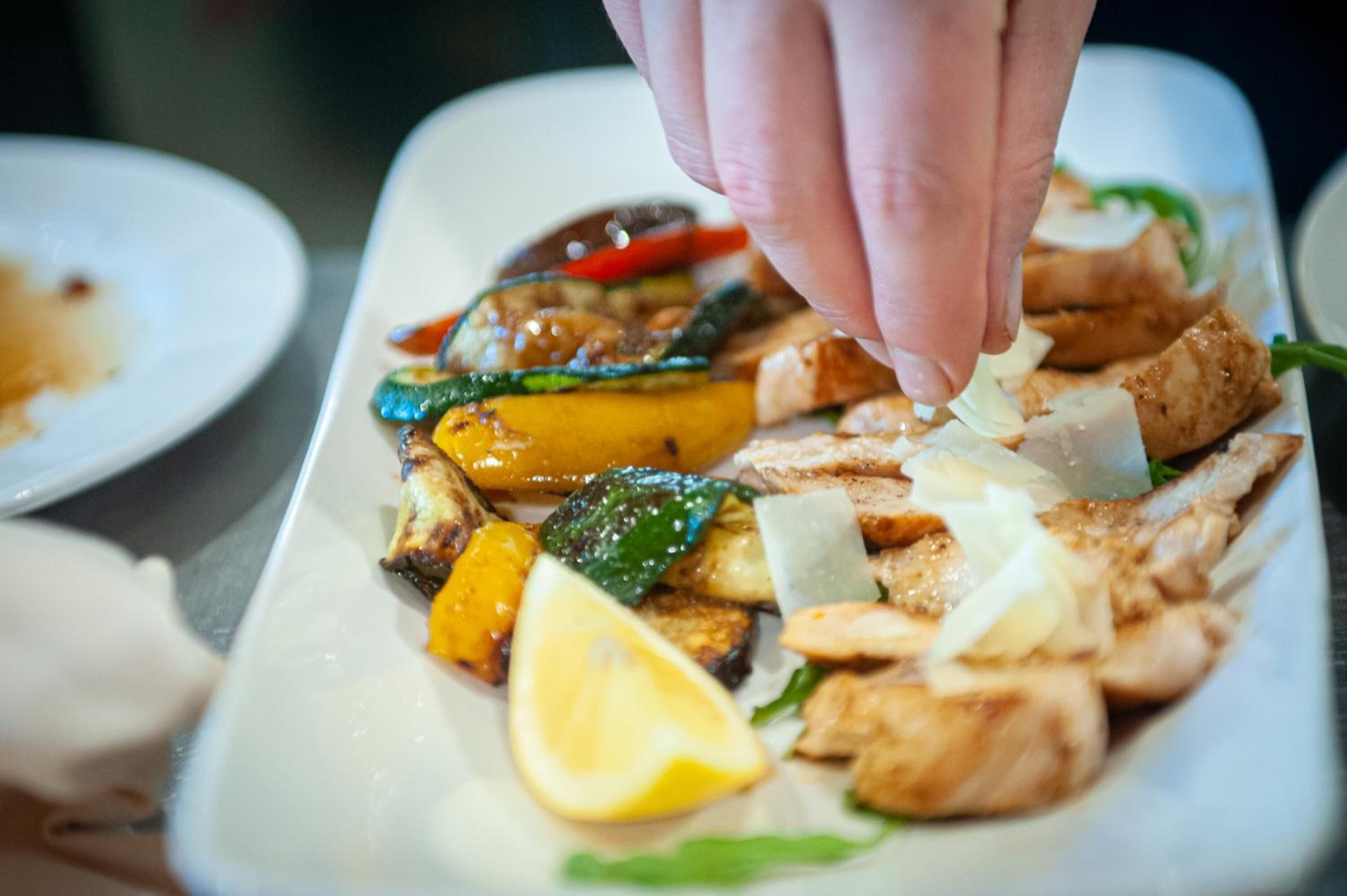 Una mano colocando un gajo de limón sobre un plato de verduras y pollo a la parrilla.