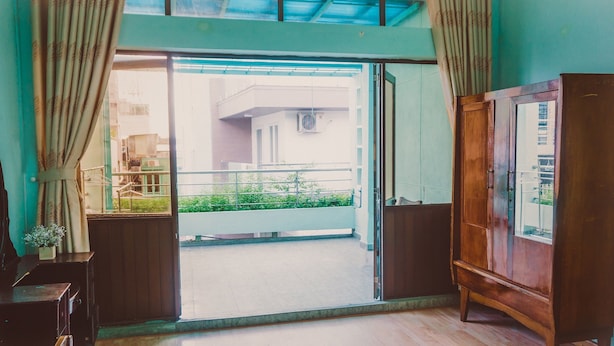 A room with a sliding glass door leading to a balcony, a wooden wardrobe, and a mirror on a dresser. - Homestay Sunny's House (Ho Chi Minh City)