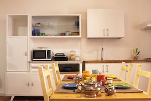 A compact kitchen with white cabinets, a microwave, and a dining table set with plates, cups, and a teapot. - B&B Dietro La Cattedrale (Palermo)