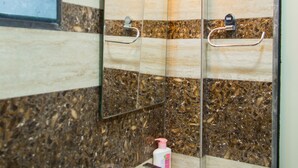 A bathroom with a marble wall, a sink, a mirror, and a towel rack. - Hotel Tourister (Mumbai)