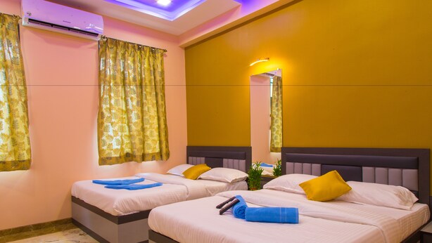 A hotel room with two beds, each with a headboard, a mirror, and a small plant on the nightstand. - Hotel Tourister (Mumbai)